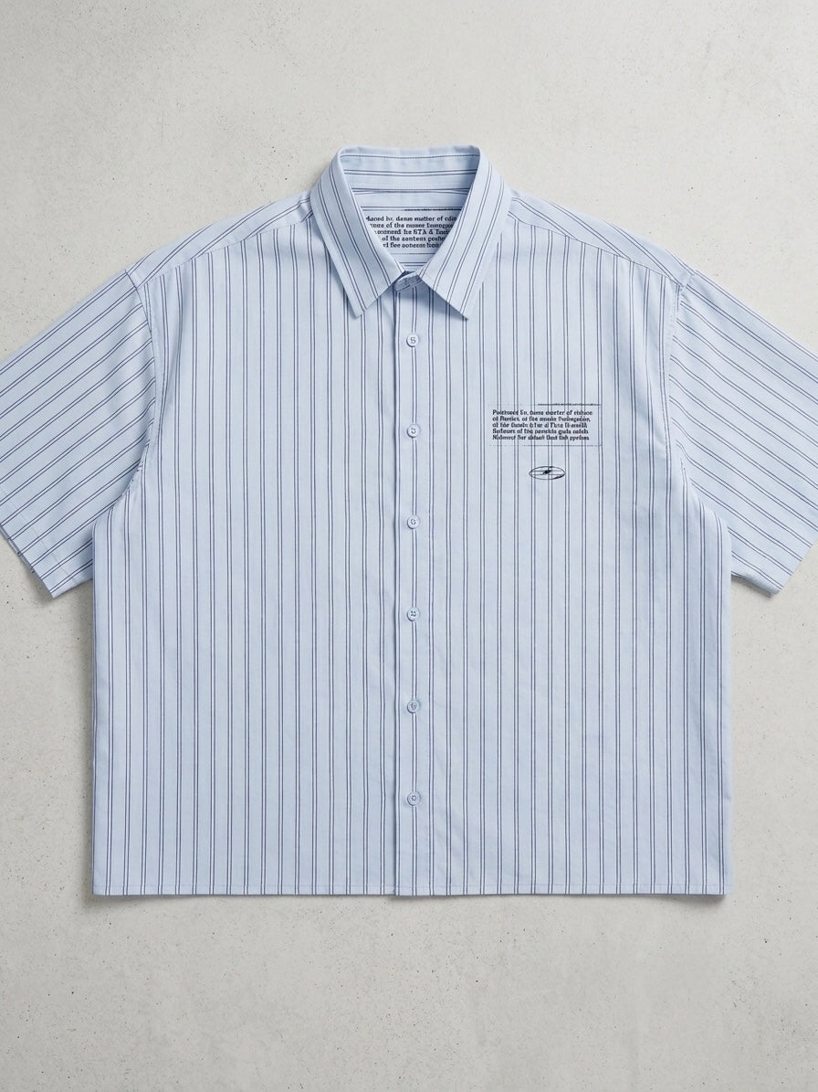 A short-sleeve button-up shirt with vertical light blue and white stripes, featuring a small embroidered logo and text on the left chest, laid flat against a textured light gray background.