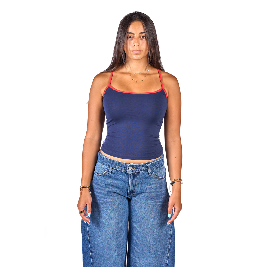 A woman modeling a navy blue ribbed tank top with red trim on the straps and neckline, paired with blue jeans, against a solid white background.